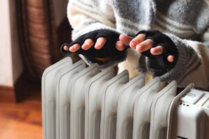 A person heating their hands at home over a plug-in, electric oil-filled radiator.